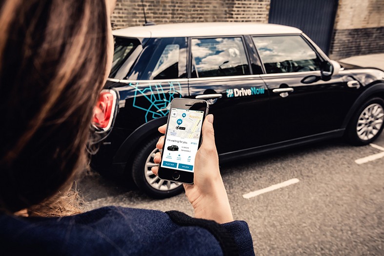 Jonge vrouw die een DriveNow wagen reserveert met haar smartphone drivenow-brussel