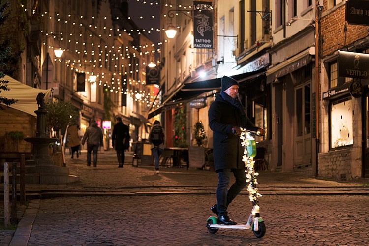 A stylish man on an electric step in the iulluminted streets of Brussels kbc-brussels-wishes